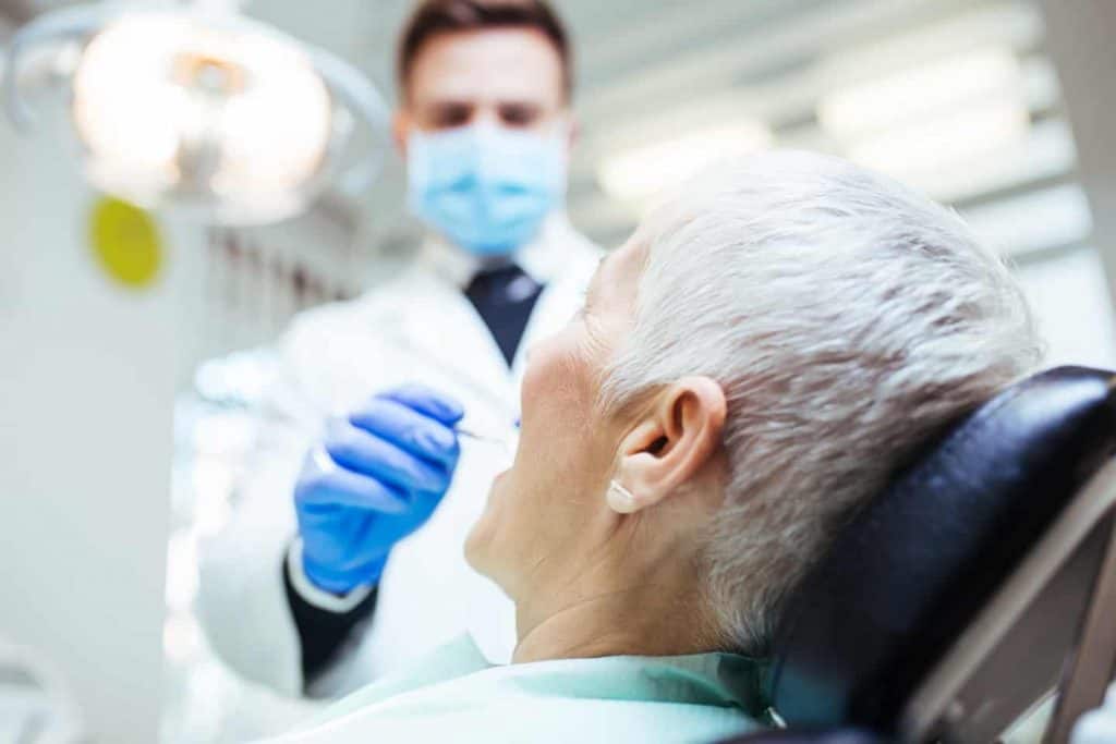 image of dentist leaning over man on dental chair while examining his mouth